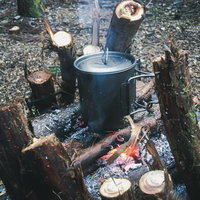 焚き火台で温める鍋を炎が照らす野外調理風景の写真