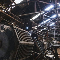 抜け落ちた天井と錆びた大型ギアが残る製紙工場内部の写真
