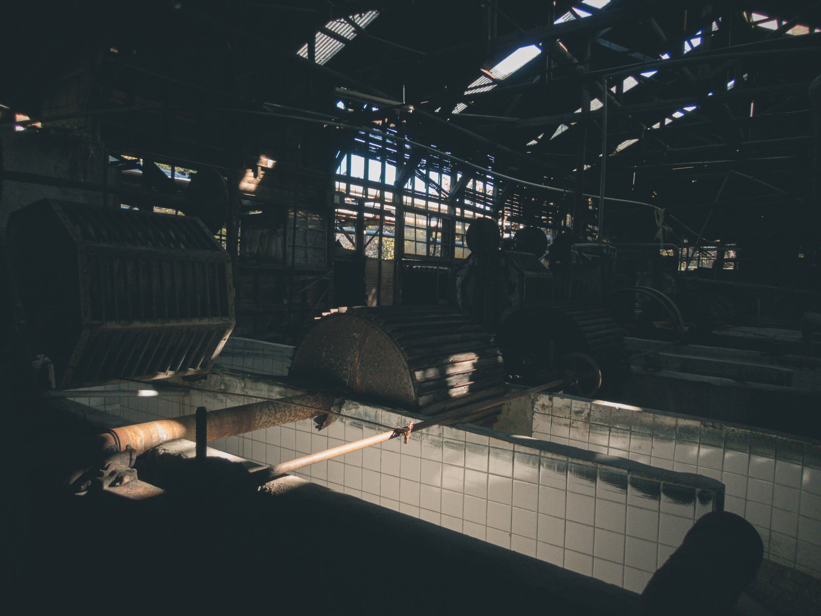 錆びついた梁とタイル壁が見える薄暗い廃工場の内部