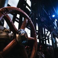 暗い廃工場内で青く照らされた赤い手動弁とボルトの写真