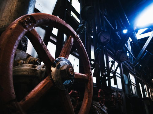 暗い廃工場内で青く照らされた赤い手動弁とボルト