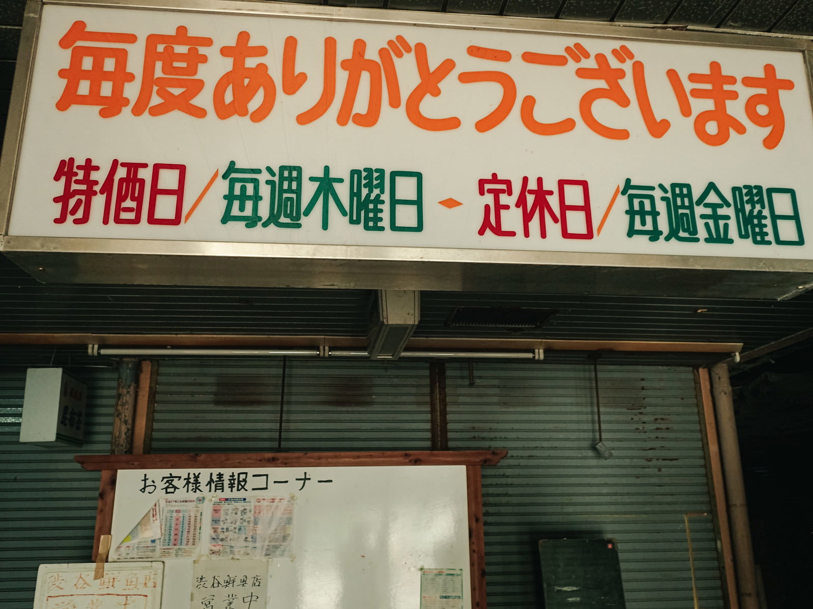白い看板に赤い大きな文字で「毎度ありがとうございます」と書かれた看板、シャッター街の背景