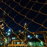 金網フェンス越しに見える工場夜景と産業施設の照明の写真