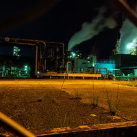 フェンス越しに見るオレンジ色の工場夜景と煙突の写真