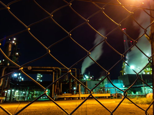金網越しに見るオレンジ色の照明が照らす工場夜景