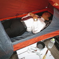 テント生活をはじめた会社員が寝袋で横になるの写真
