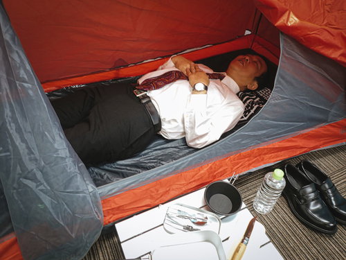 テント生活をはじめた会社員が寝袋で横になる