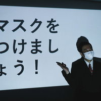 「マスクをつけましょう！」啓蒙スライドと説明する男性の写真