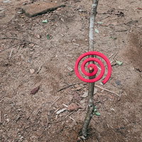 土の地面に刺した枝にかけた赤い渦巻の蚊取り線香の写真