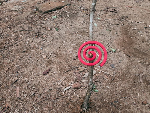 土の地面に刺した枝にかけた赤い渦巻の蚊取り線香