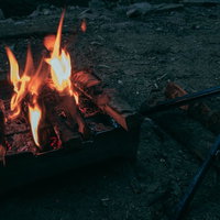 キャンプファイヤーで燃え上がる薪の炎とトングの写真