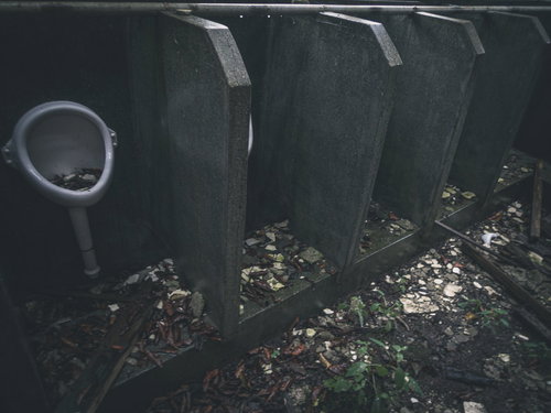 瓦礫と落葉に覆われた廃墟の男子トイレ