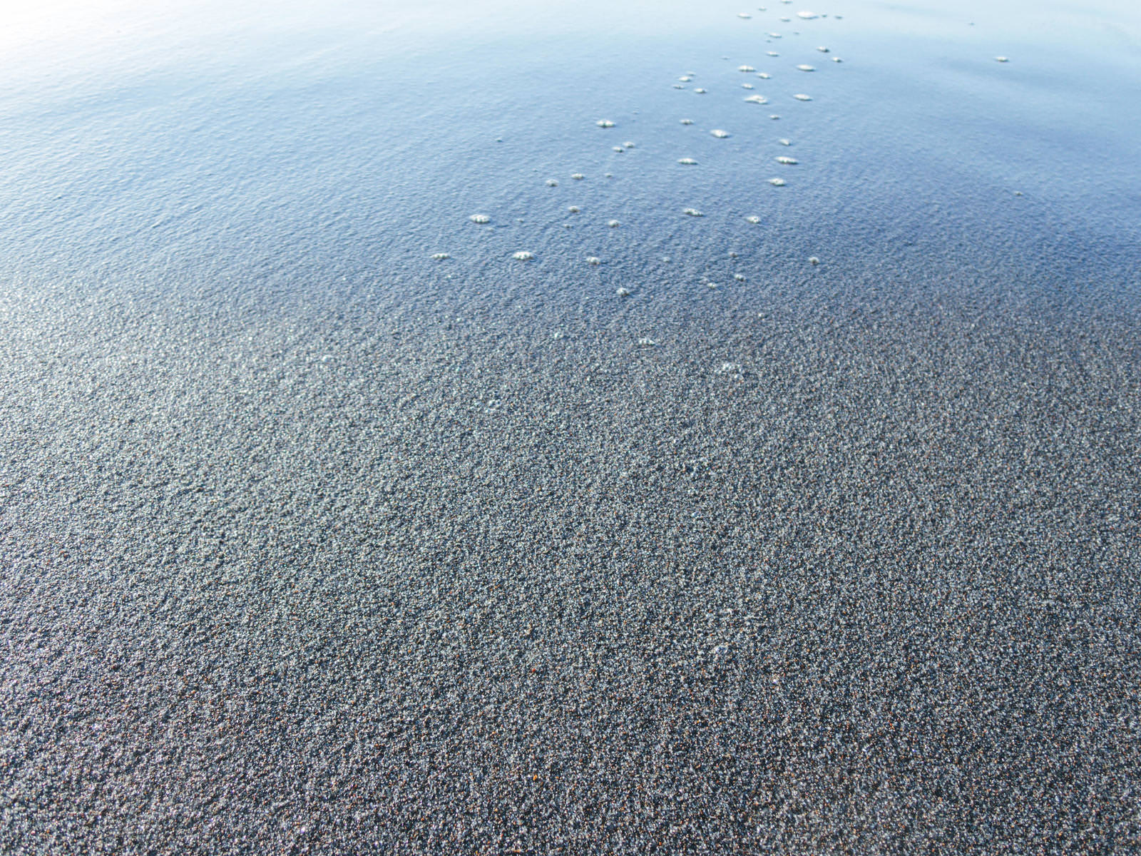 青い海水が砂浜に打ち寄せて白い泡を残しながら引いていく波の様子