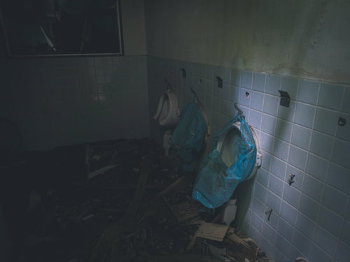 廃墟の男子トイレ内部 壊れた便器と剥がれた白タイル
