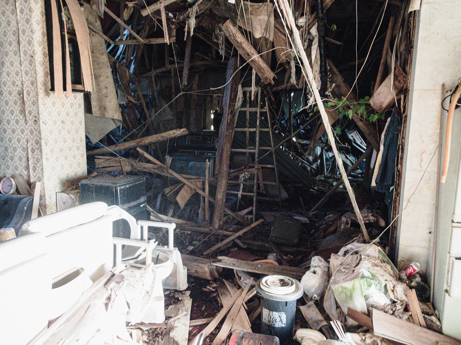 屋根が崩れ落ち、室内に瓦礫や木材が散乱している廃家