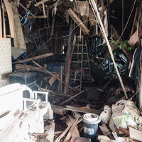 屋根が崩れ落ちた瓦礫まみれの廃家と倒壊した建物跡の写真