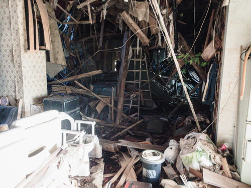 屋根が崩れ落ちた瓦礫まみれの廃家と倒壊した建物跡