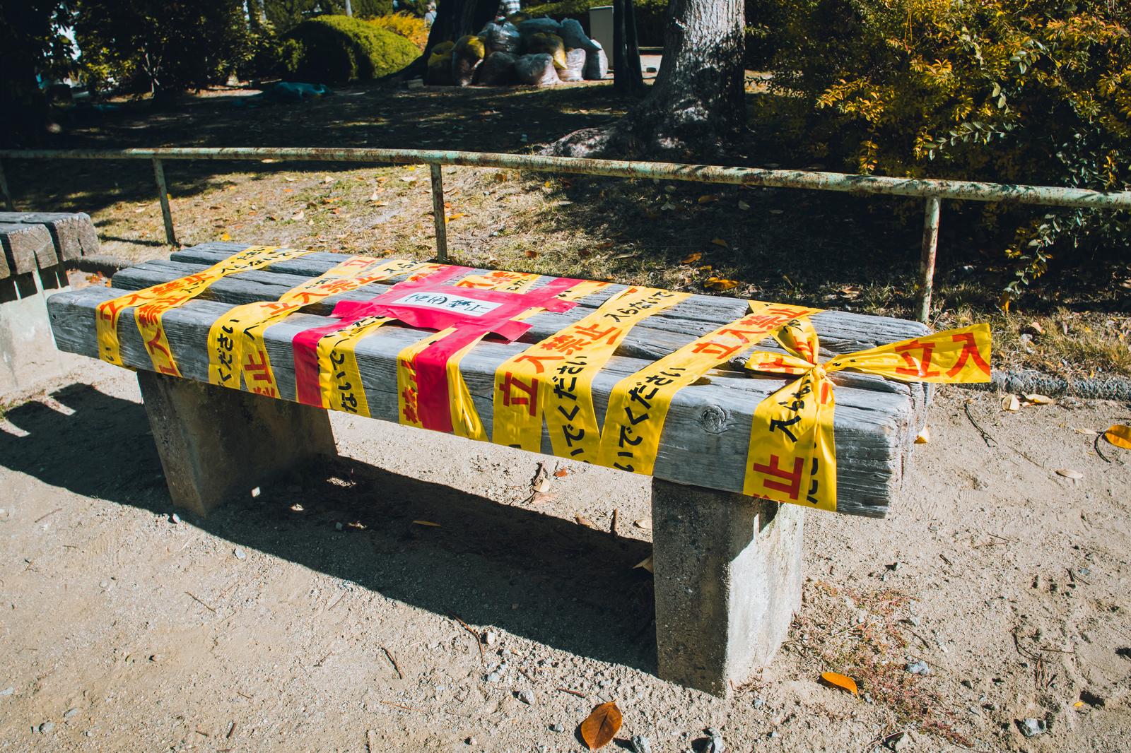 A wooden park bench wrapped multiple times with yellow tape marked with no entry warnings