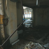 床に散らばった瓦礫とぶら下がる錆び付いた配管の写真