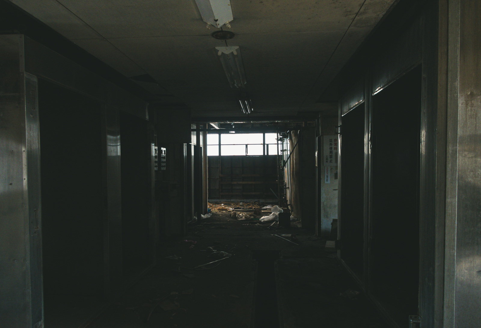 瓦礫が散乱したボロボロの廃墟廊下を暗がりの中で撮影した写真