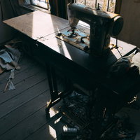 廃屋の窓から差す光に照らされたミシンの残骸の写真