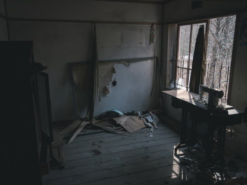 廃屋に取り残された古いミシンと荒廃した室内