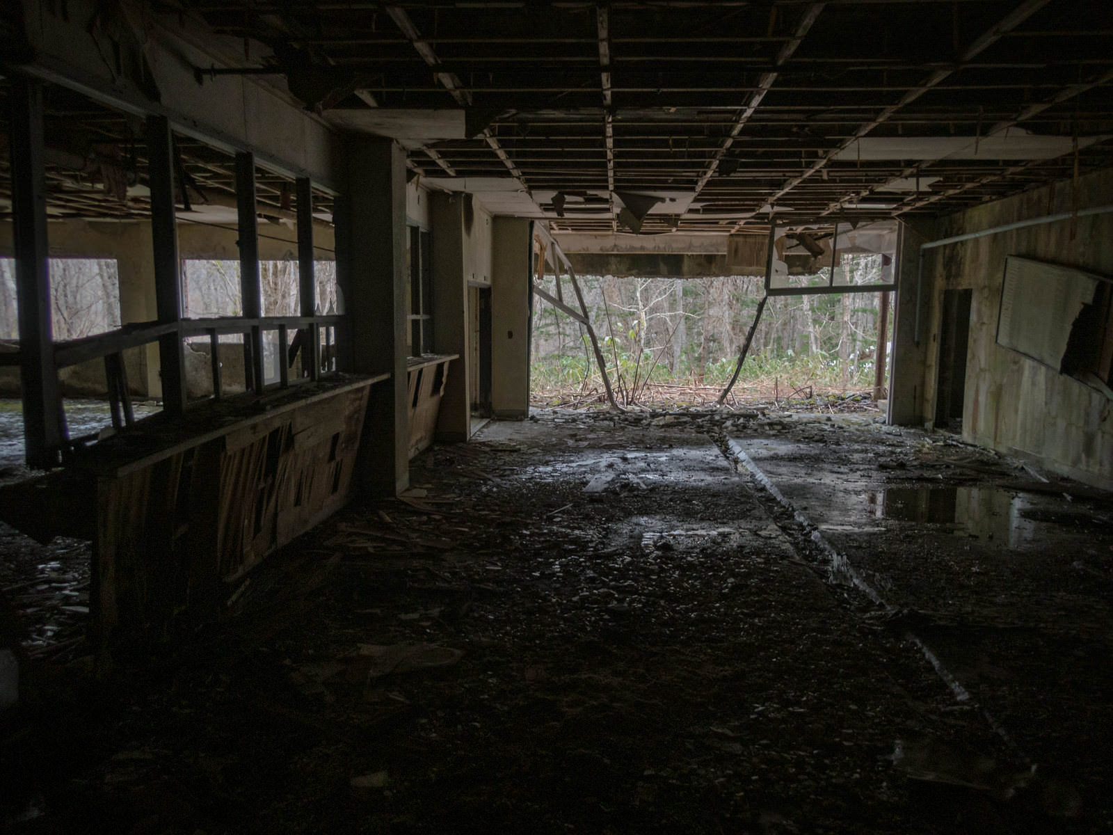 廃墟の室内で崩れ落ちた天井と床に溜まった水溜りが見える暗い空間