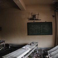 朽ちた廃屋の教室に残された黒板と机椅子、神棚の写真