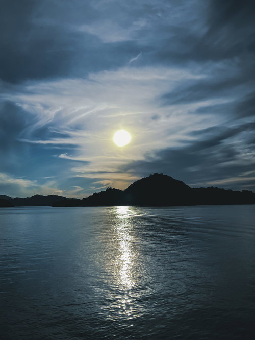曇り空に浮かぶ太陽とレイラインが水面に映る風景
