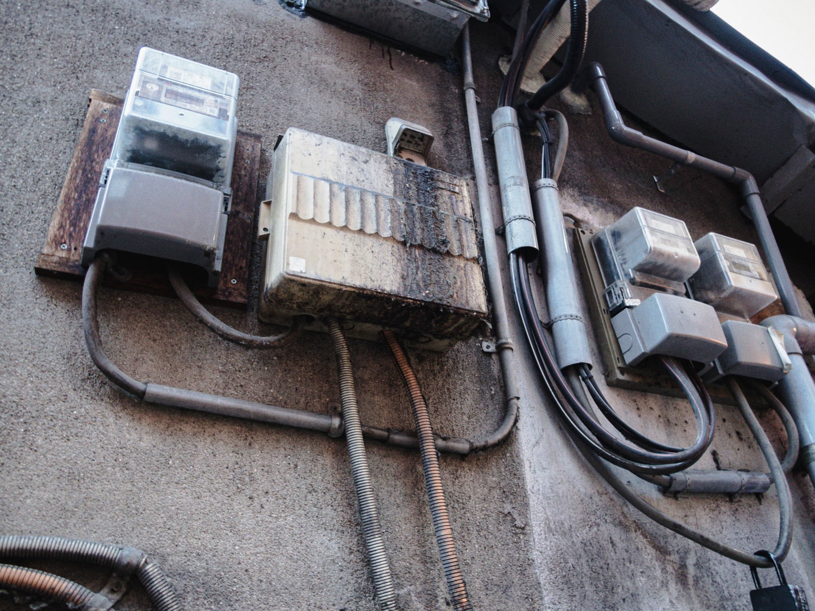 老朽化した室外の電気メーターと分電盤が壁に設置されている