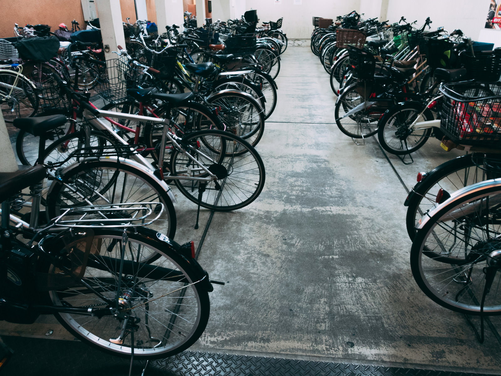 コンクリートの駐輪場に黒い自転車が規則正しく整列している様子