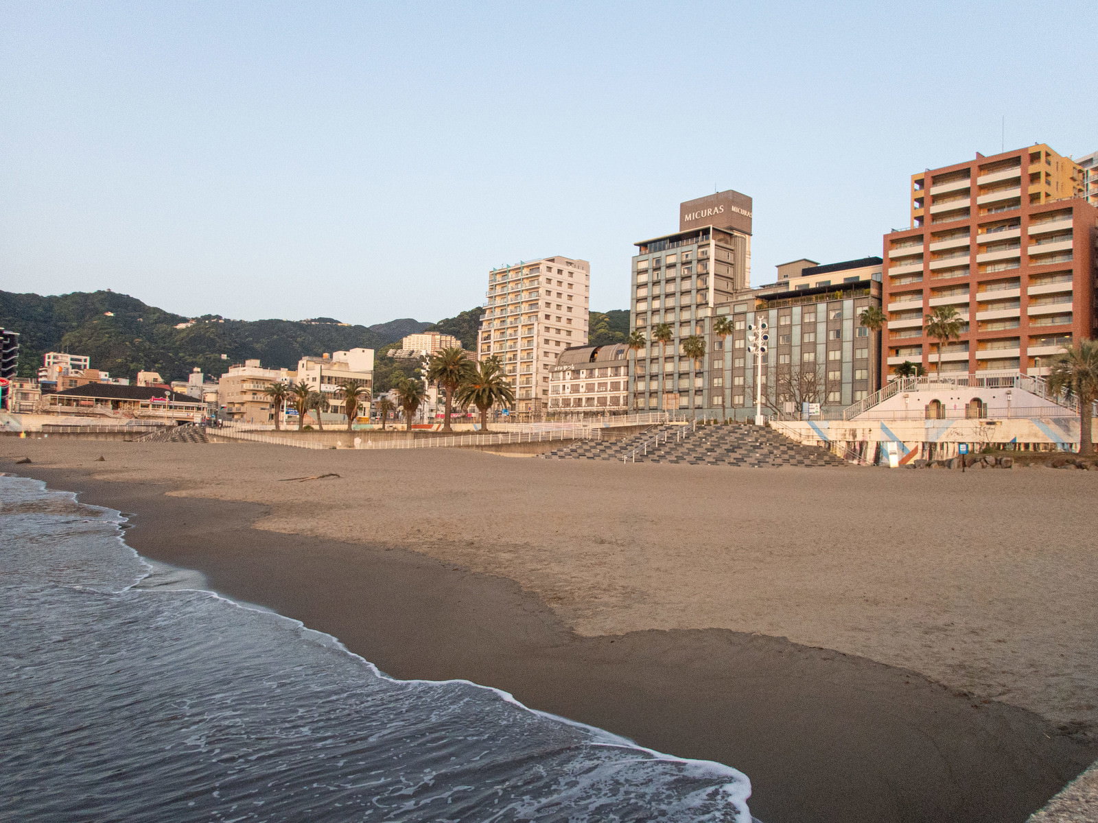 熱海の海岸に白い波が打ち寄せる砂浜と背景に立ち並ぶホテル群