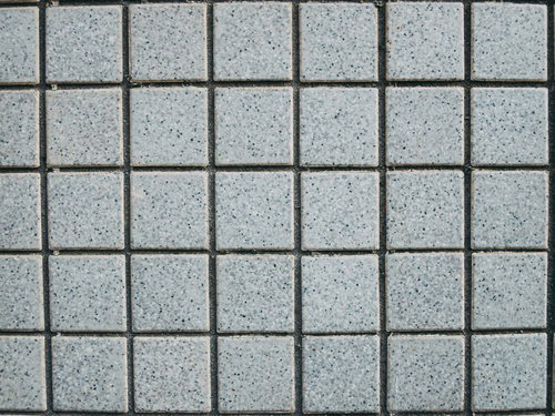 細かい粒が散るグレーの正方形タイル壁のテクスチャー