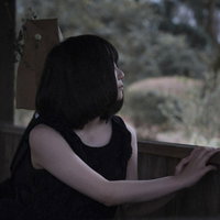 窓辺で外を見つめる闇系女子の横顔、暗い室内で物思いにふけるの写真