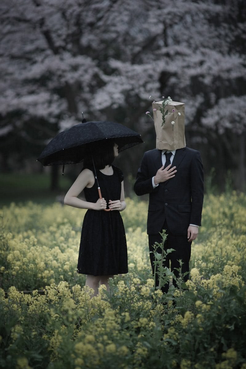菜の花畑で黒い服を着た男性と女性が向き合って話している