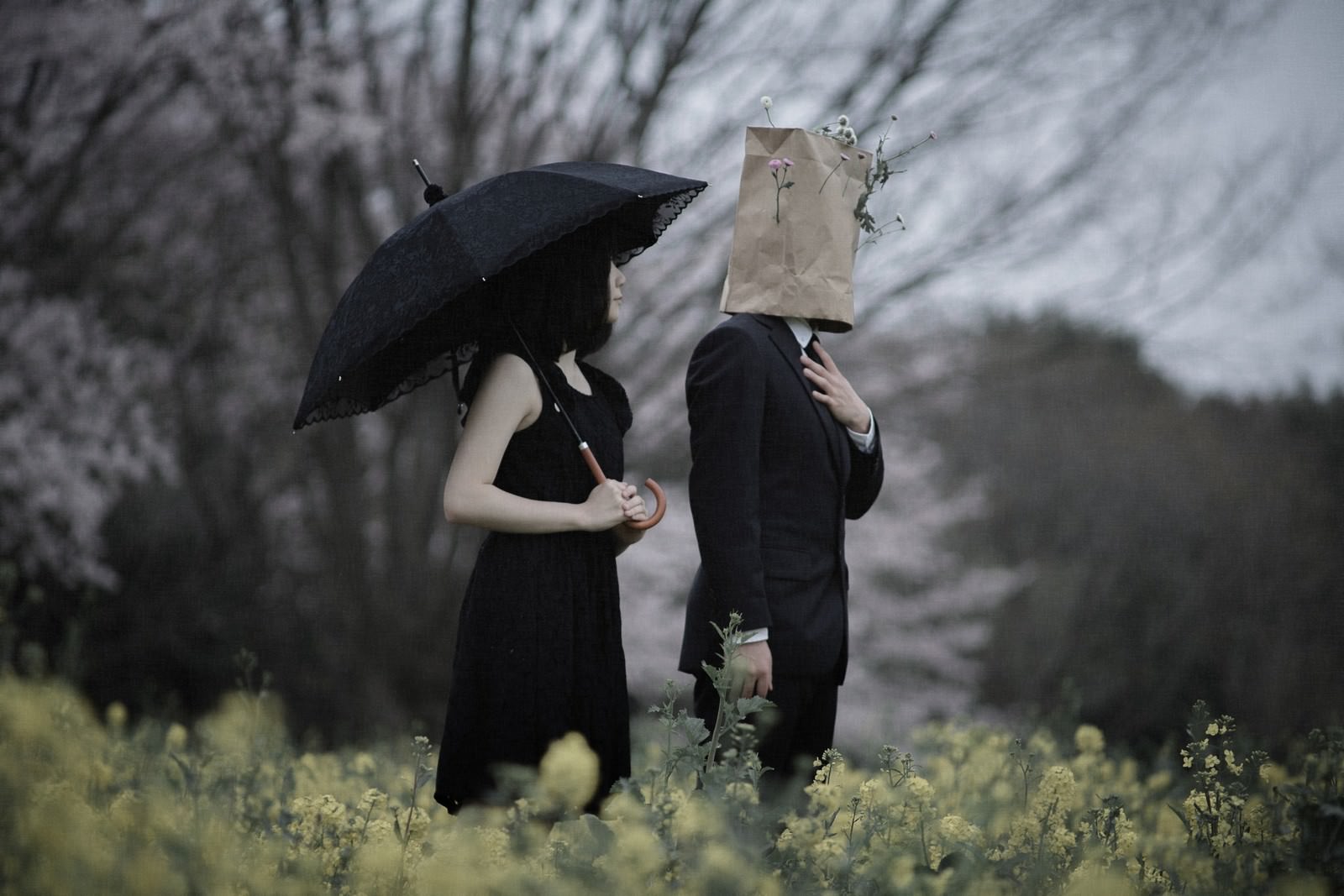 菜の花畑で紙袋を被って黙祷する恋人2人の後ろ姿