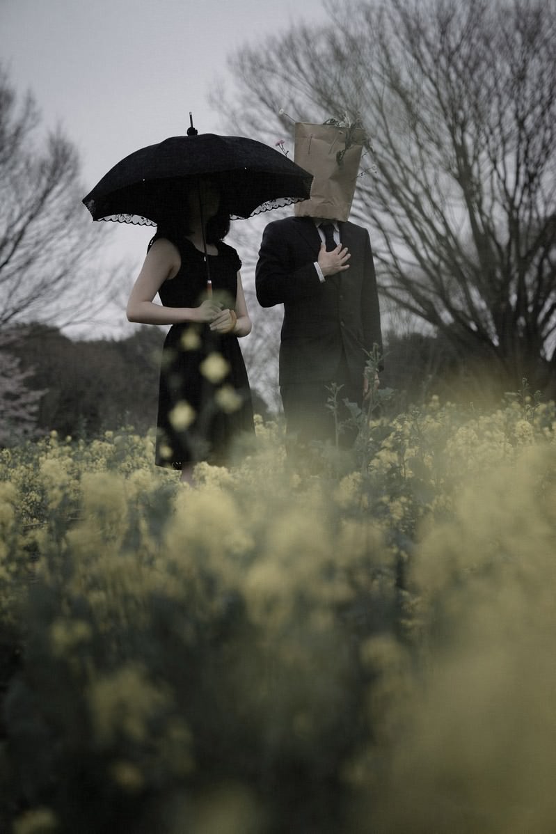 菜の花畑で傘を差して黙祷する男女のシルエット