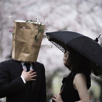 紙袋をかぶった紳士が日傘の女性に挨拶するユニークなシーンの写真