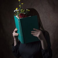 緑色の本で顔を隠す読書女性のポートレートの写真