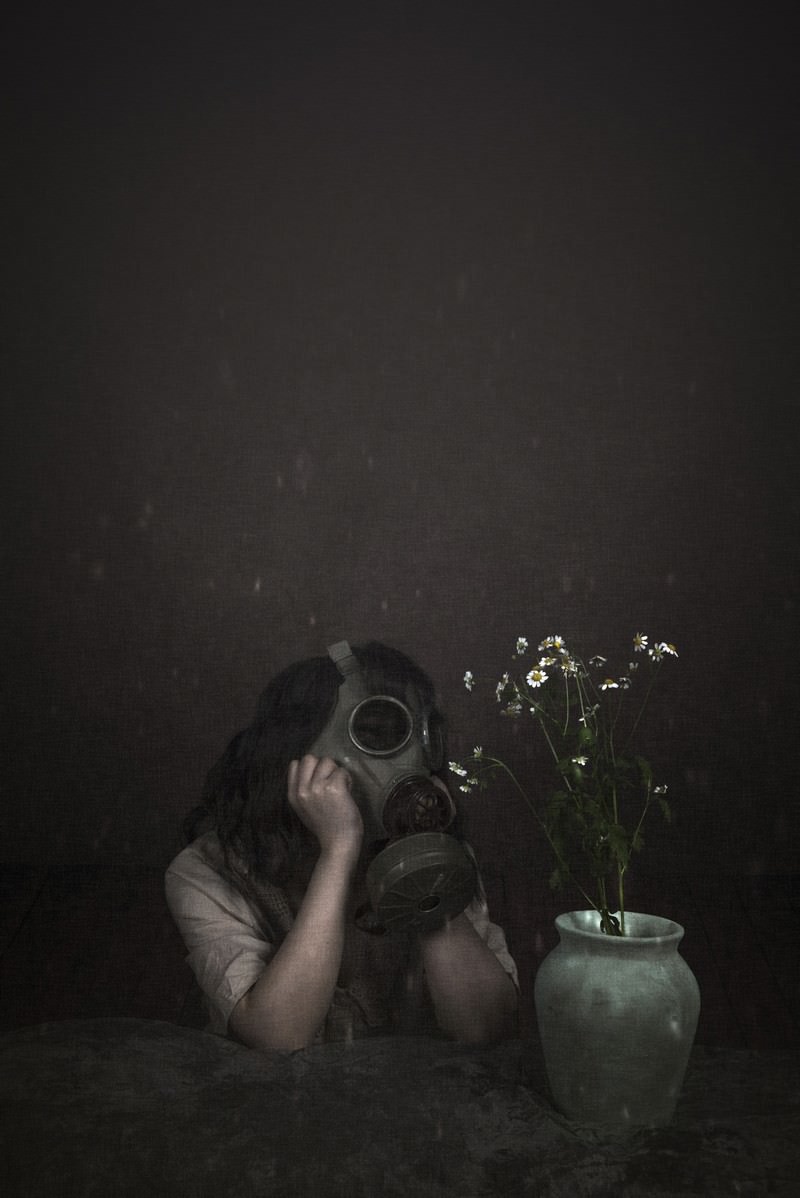 暗い背景の中で被り物をした少女が花瓶の一輪の花を見つめている