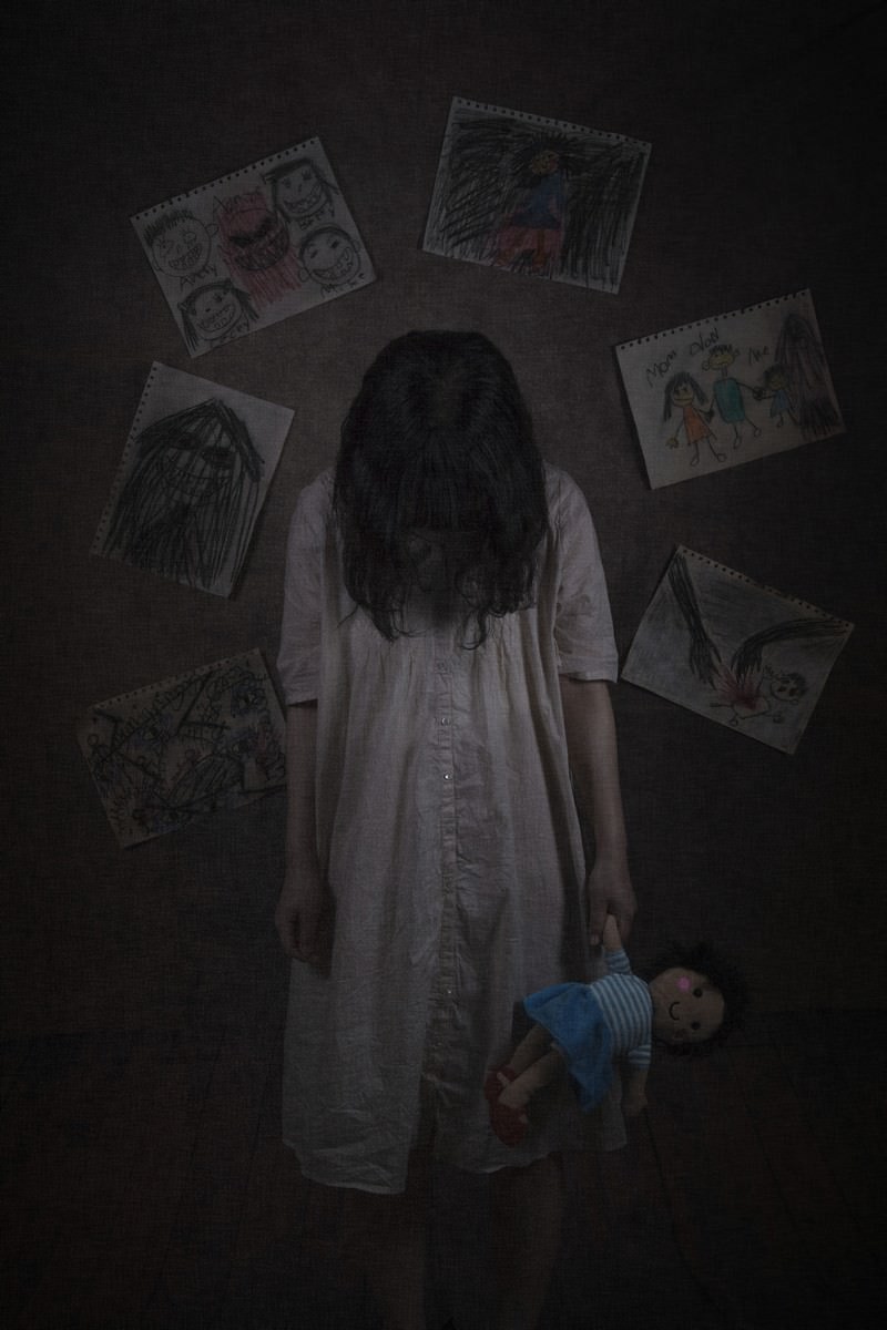 暗い部屋で白い服を着た女性がぬいぐるみと一緒に佇んでいる様子