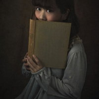 本で顔を隠しながら怯えた瞳で見つめる女性の写真