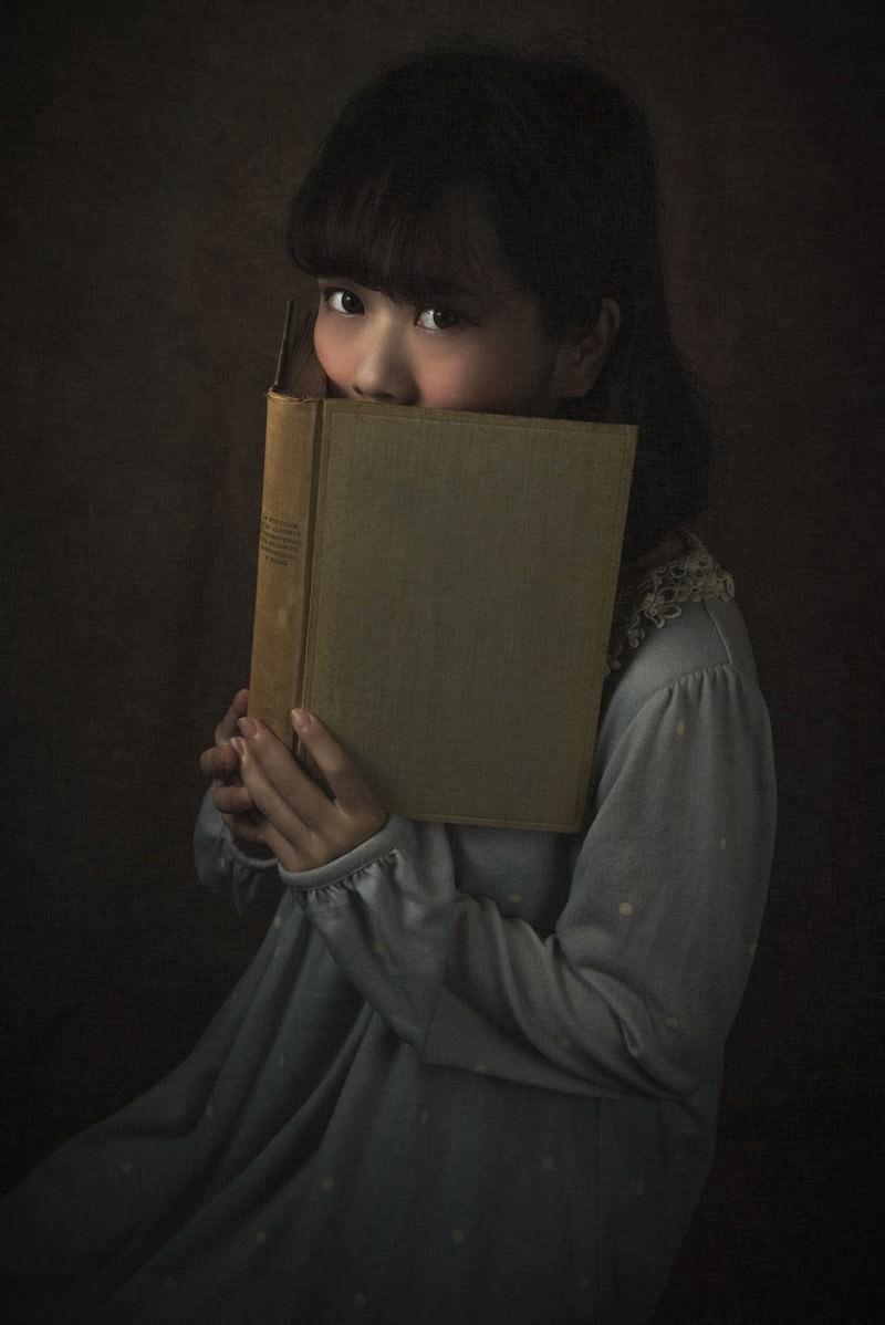 本で顔を隠しながら上目遣いでこちらを見つめる女性