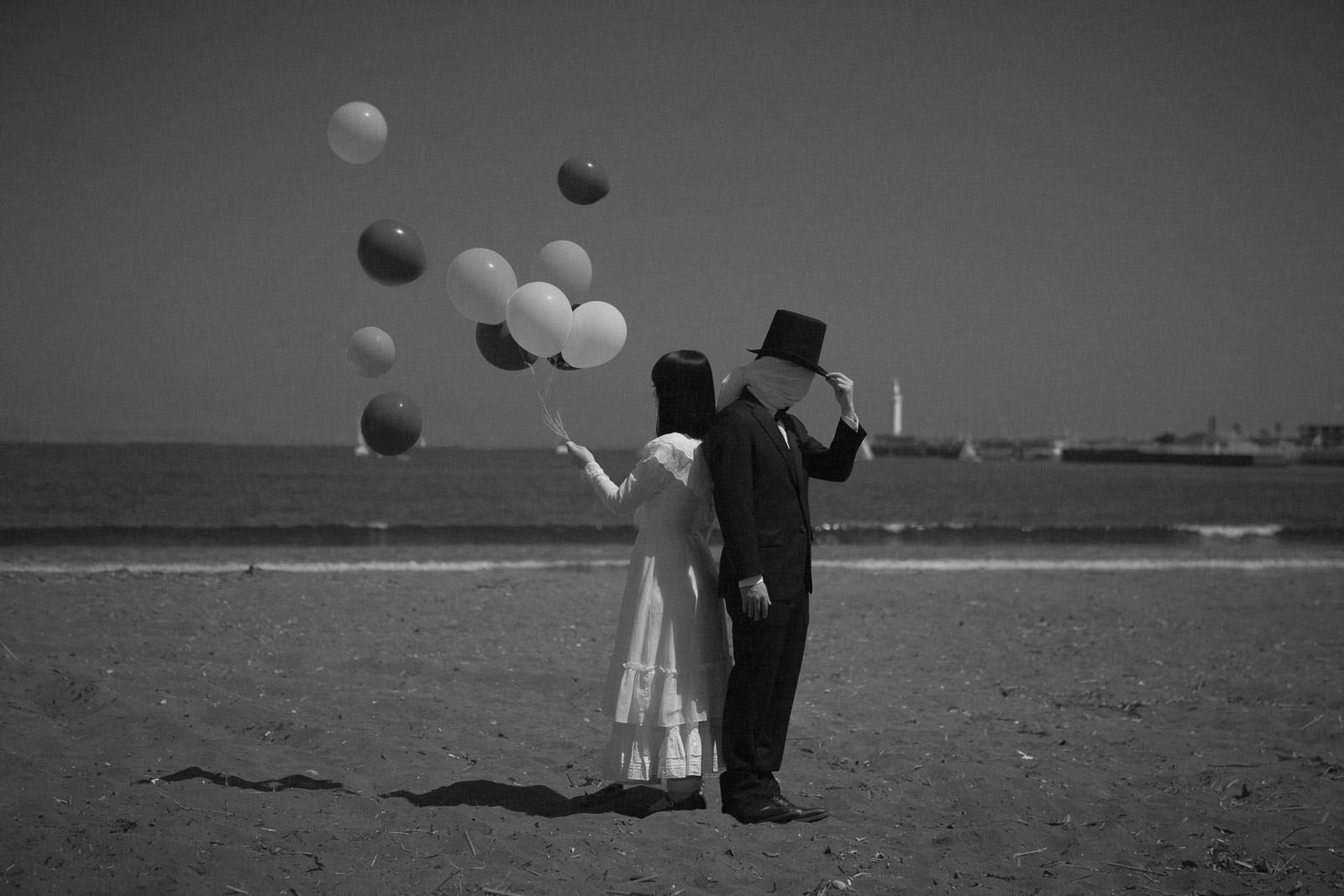 海辺で風船を空に向かって飛ばしているカップルのモノクロ写真