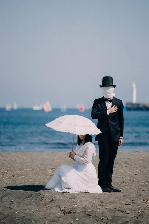 覆面をした男子と白いドレスのお嬢様が砂浜で向き合う