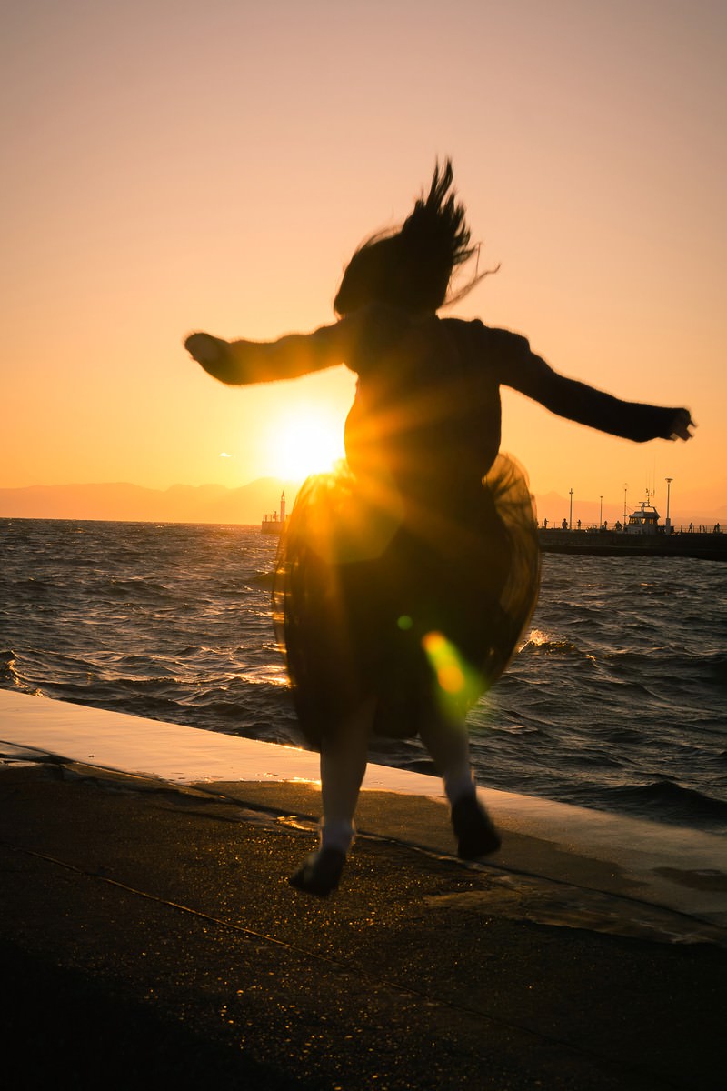 夕焼けの海辺で両手を広げてジャンプする人のシルエット