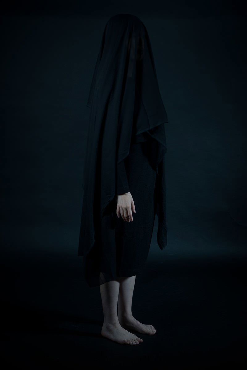 Person standing in the dark, covered with a black cloth