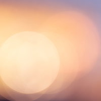 オレンジから淡いピンクへのグラデーションに浮かぶ柔らかな丸ボケの写真