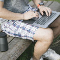 公園のベンチで音楽を流しながらノートパソコンで作業するエンジニアの写真