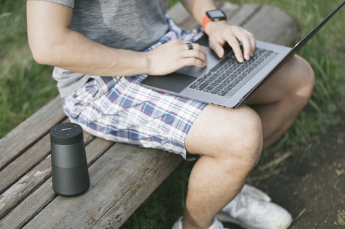 公園のベンチで音楽を流しながらノートパソコンで作業するエンジニア